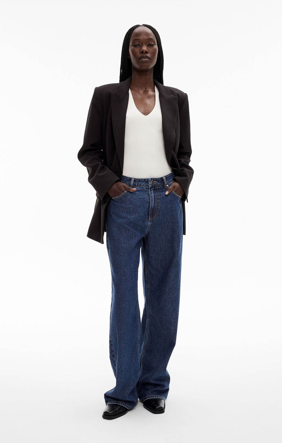 Woman in black blazer, white knit tank top, blue denim jeans and black boots