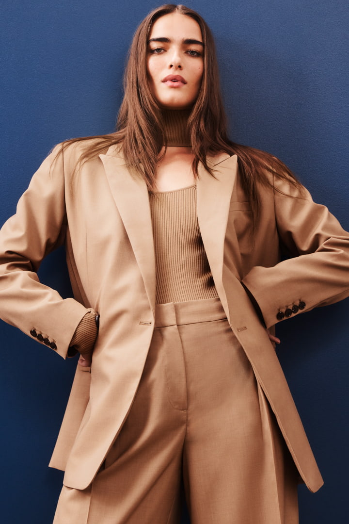 Model in camel double breasted boxy blazer, camel high neck knit bodysuit, camel pleat detail pant and patent black kitten mules