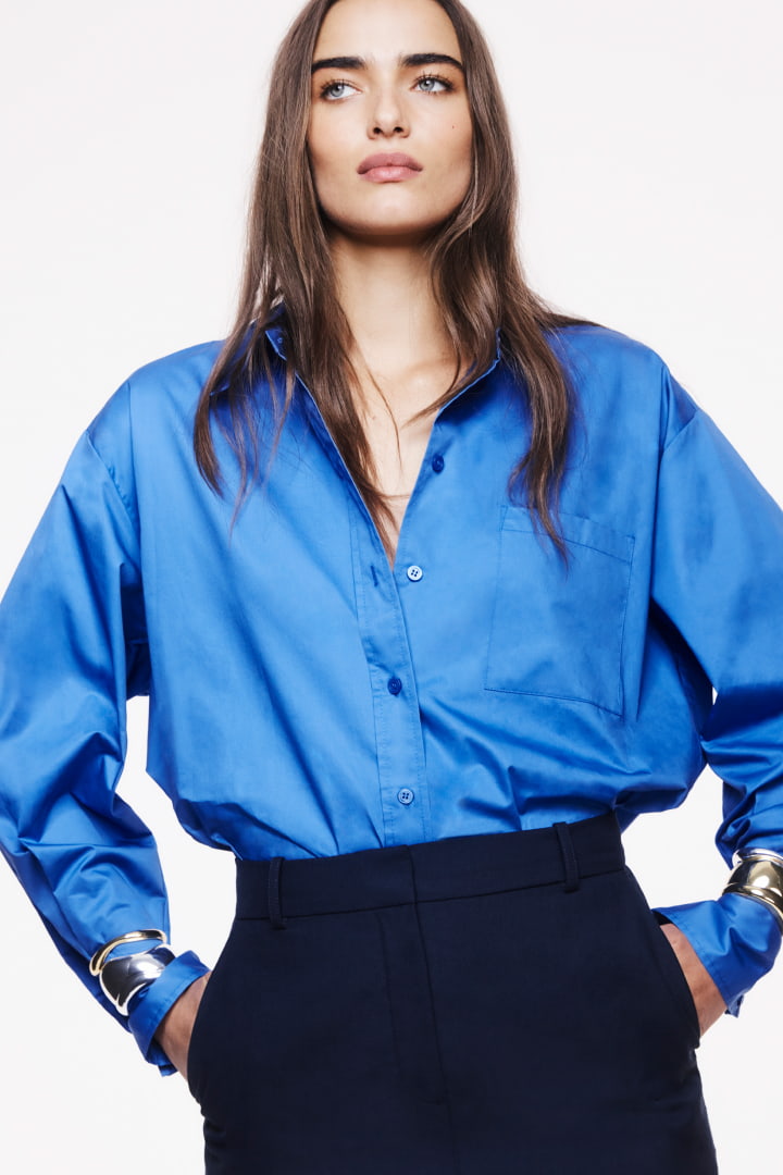 Model in blue organic cotton oversized shirt, navy wool mini skirt and patent black kitten mules